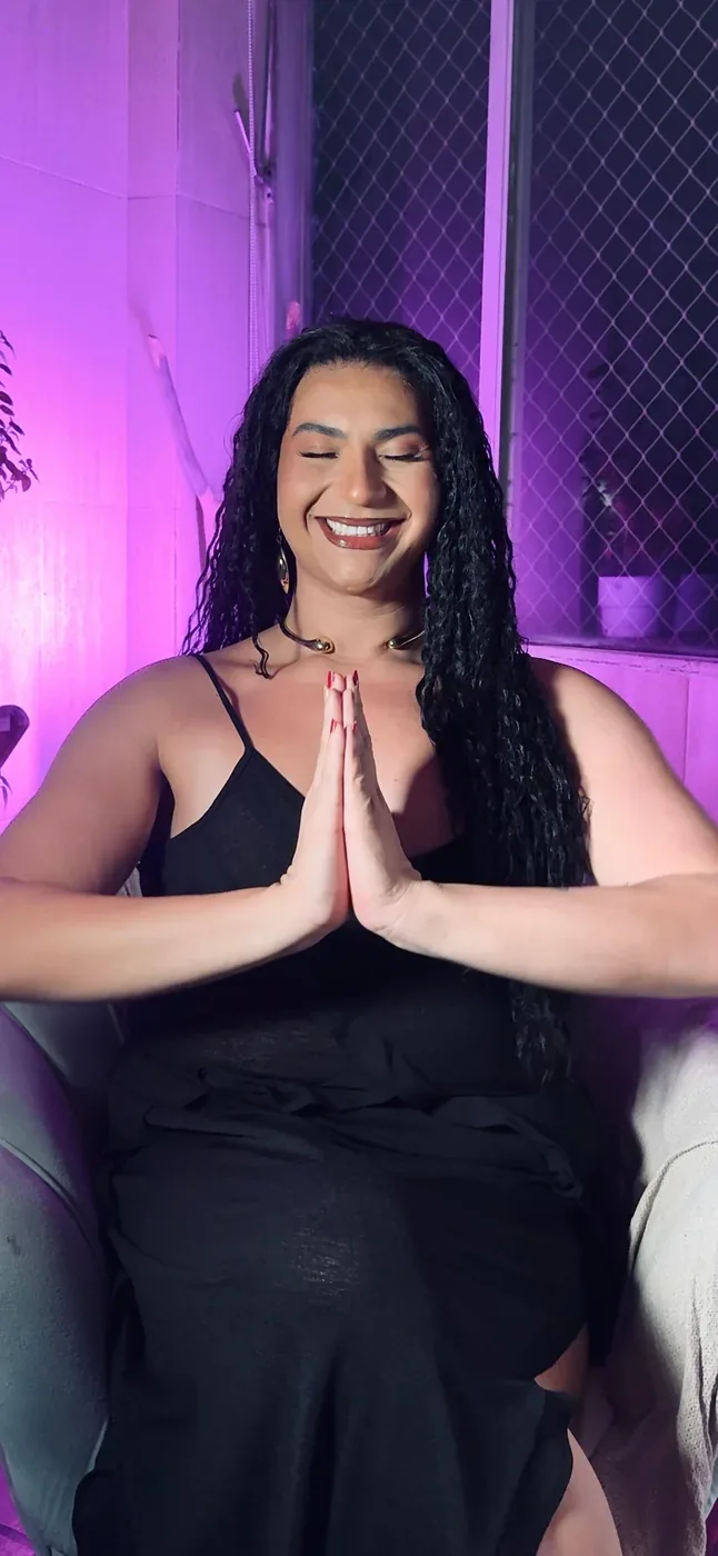 Mathy Lemoss de olhos fechados, com as mãos em prece, sob luz violeta