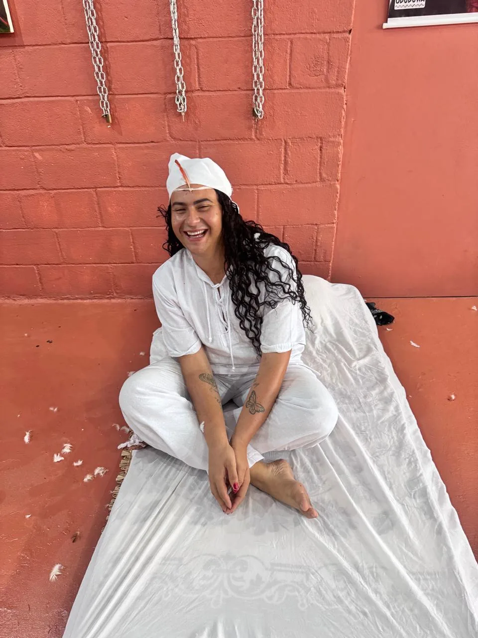 Mathy Lemoss sentada, de roupa branca, diante de uma parede vermelha