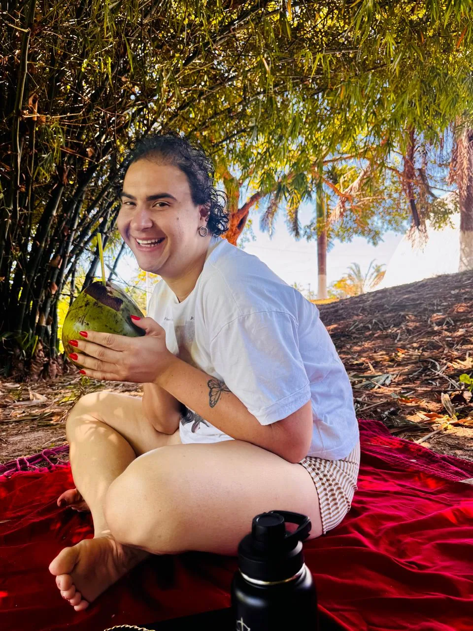 Mathy Lemoss sentada em uma canga vermelha, ao ar livre
