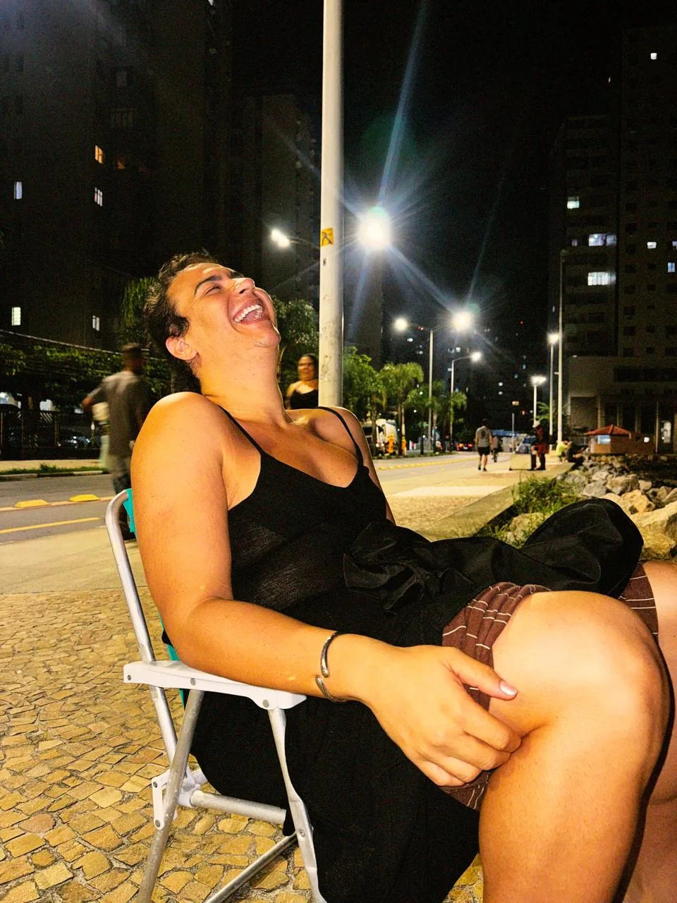 Mathy Lemoss rindo, sentada na rua à noite
